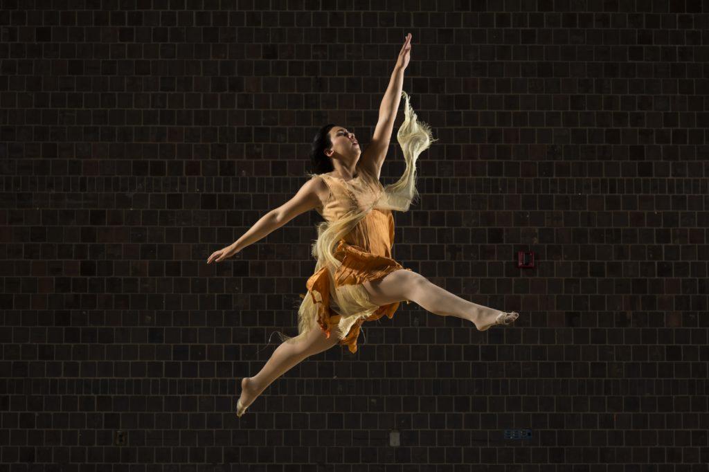 A University of Rochester student dancing on a stage, leaping in mid-air